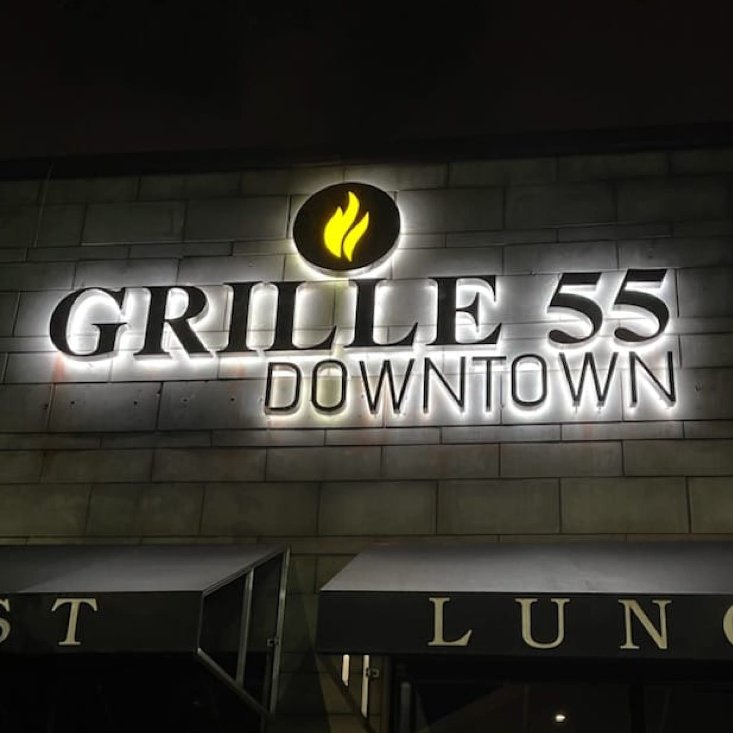 Halo-lit GRILLE 55 DOWNTOWN letters and flame logo glowing on a stone building at night