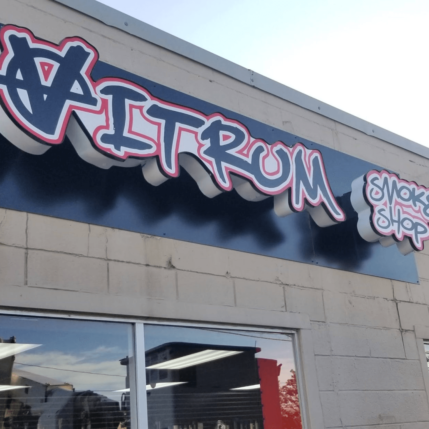 Dimensional VITRUM SMOKE SHOP letters mounted on a black backer panel above a storefront window