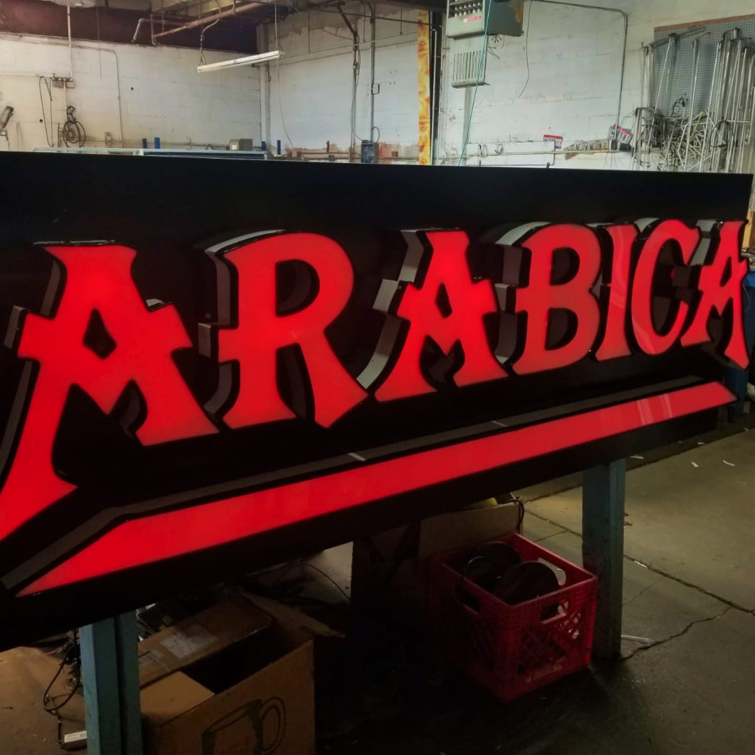 Red illuminated ARABICA channel letters lit up on a black backer inside the sign shop