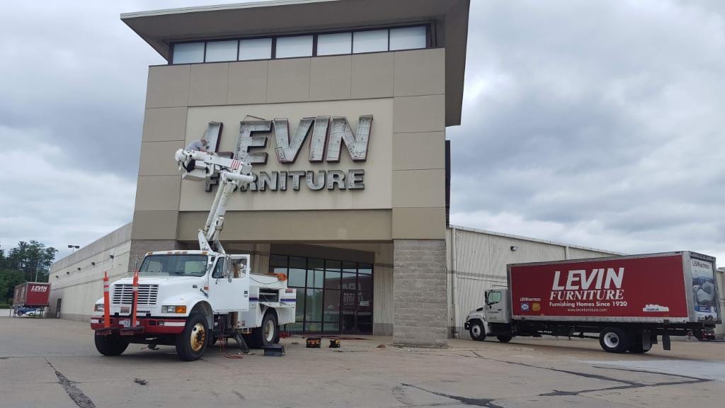Worker in a bucket truck servicing LEVIN FURNITURE letters on a storefront