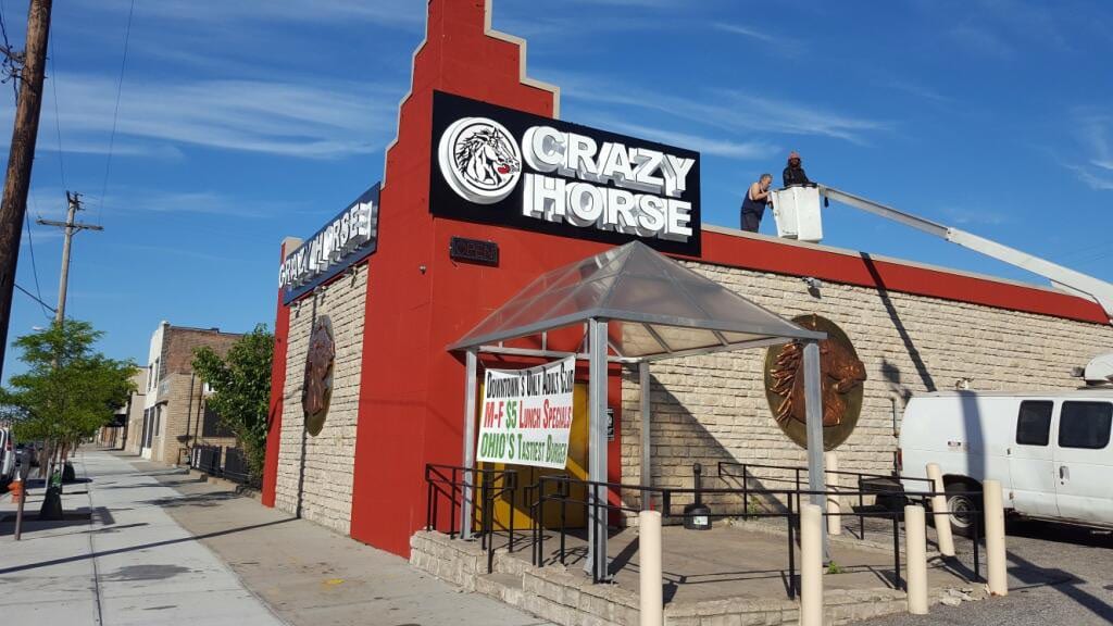 Crew in a boom lift on the roof beside a black CRAZY HORSE sign panel