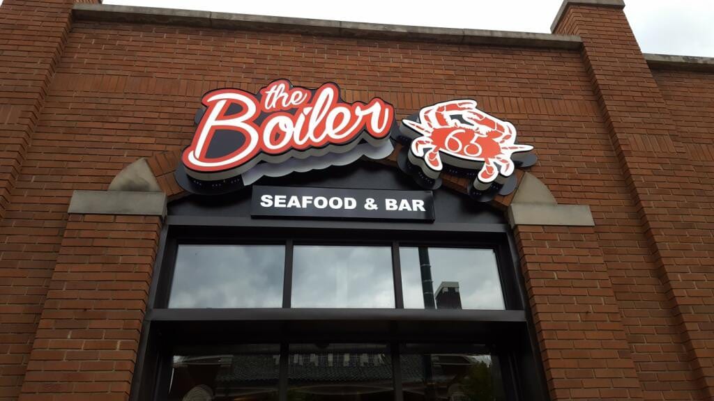 Illuminated the Boiler Seafood & Bar sign with a red crab logo mounted on a brick facade