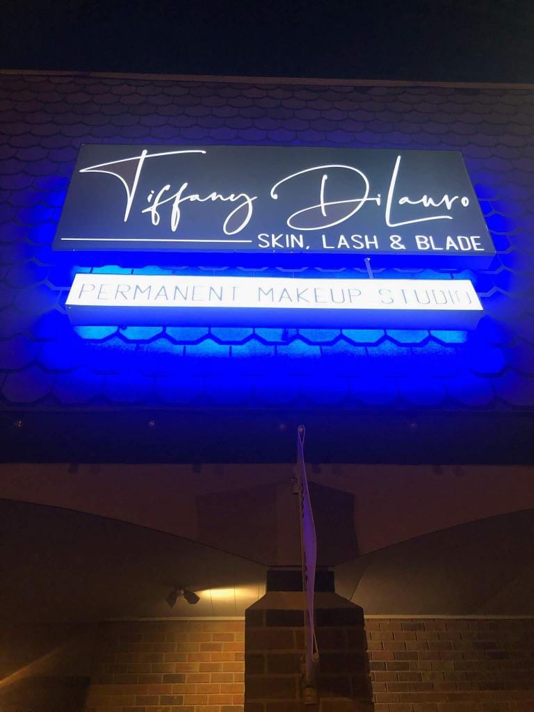 Illuminated Tiffany DiLauro Skin, Lash & Blade sign with blue backlight glow at night