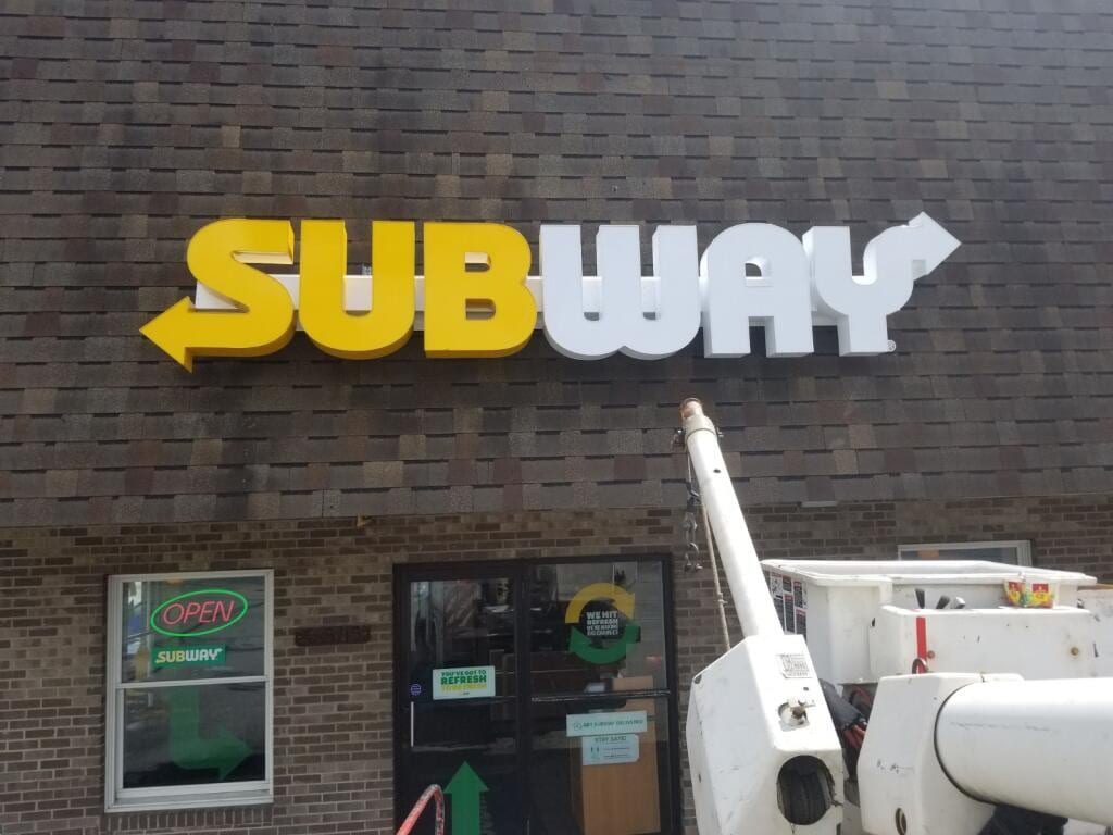 Yellow and white SUBWAY dimensional letters on a shingled facade with a bucket boom below