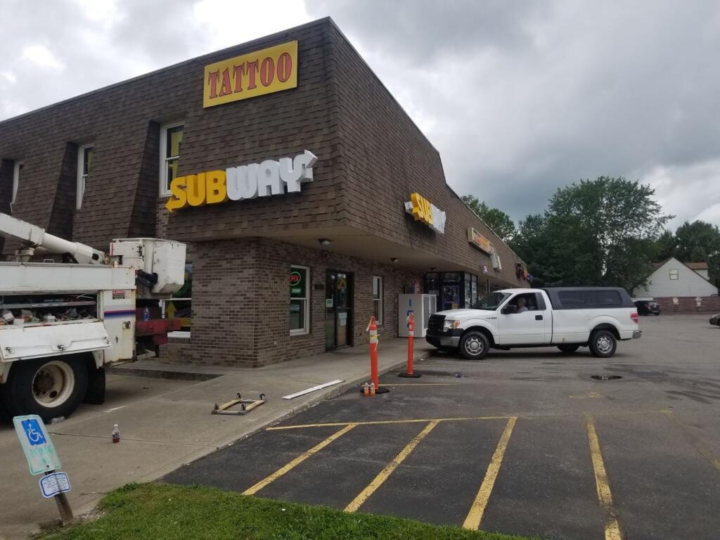 Bucket truck at a strip plaza with SUBWAY letters and a yellow TATTOO cabinet sign