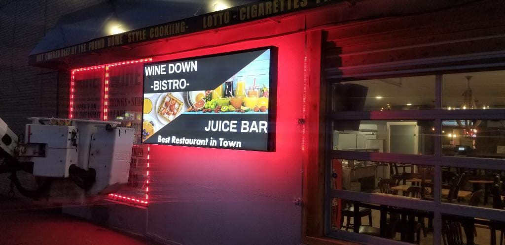 Illuminated Wine Down Bistro juice bar lightbox with red LED trim on a building at night