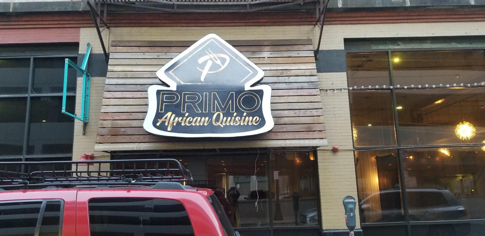 Shaped PRIMO African Quisine cabinet sign mounted on a wood plank facade