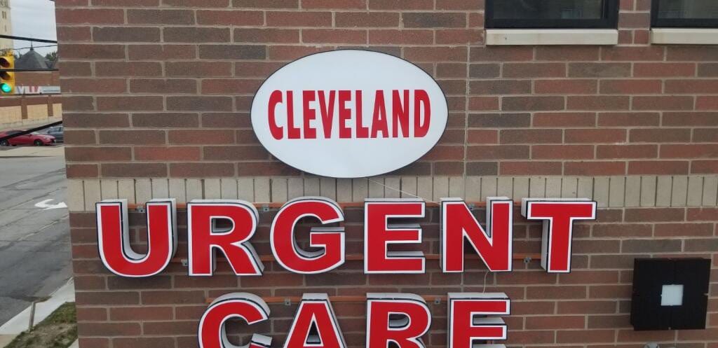 Red CLEVELAND URGENT CARE channel letters and oval cabinet mounted on brick