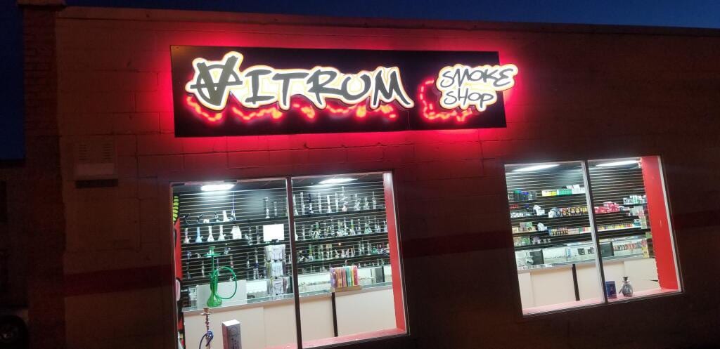 VITRUM SMOKE SHOP letters glowing red on a black panel above a lit storefront at night