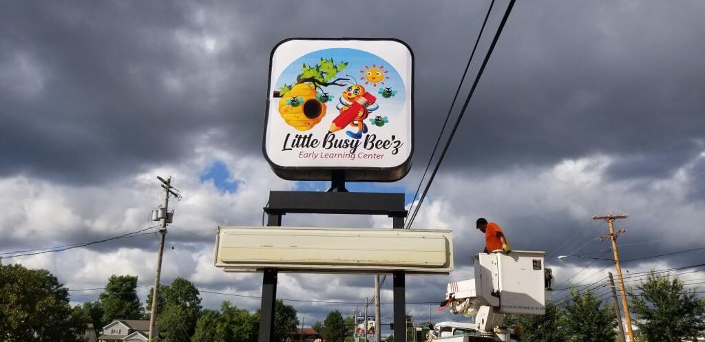 Worker in a bucket lift at a Little Busy Bee'z Early Learning Center pole sign