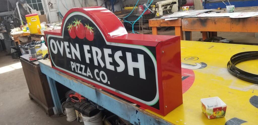 Shaped Oven Fresh Pizza Co. lightbox cabinet resting on a bench in the sign shop
