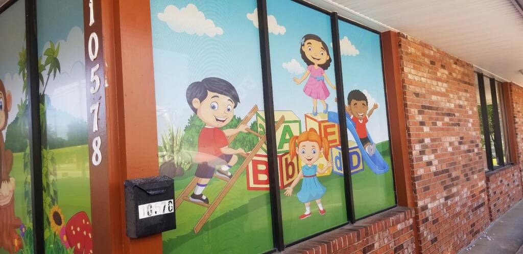 Printed window graphics of cartoon children and blocks covering a storefront's front windows