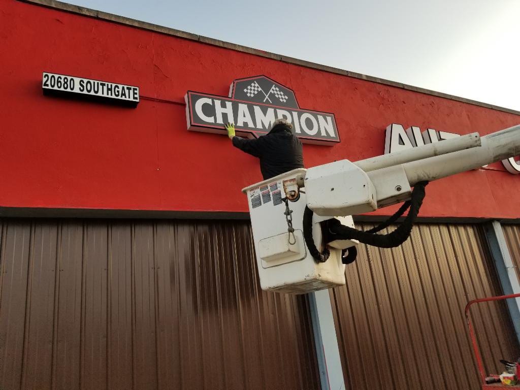 Worker in a bucket lift mounting the Champion sign on a red building fascia
