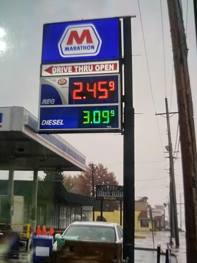 Marathon pylon sign with LED gas price digits above a fuel canopy on a rainy day
