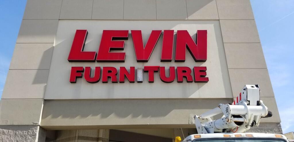 Red LEVIN FURNITURE channel letters on a stone facade with a bucket truck boom below