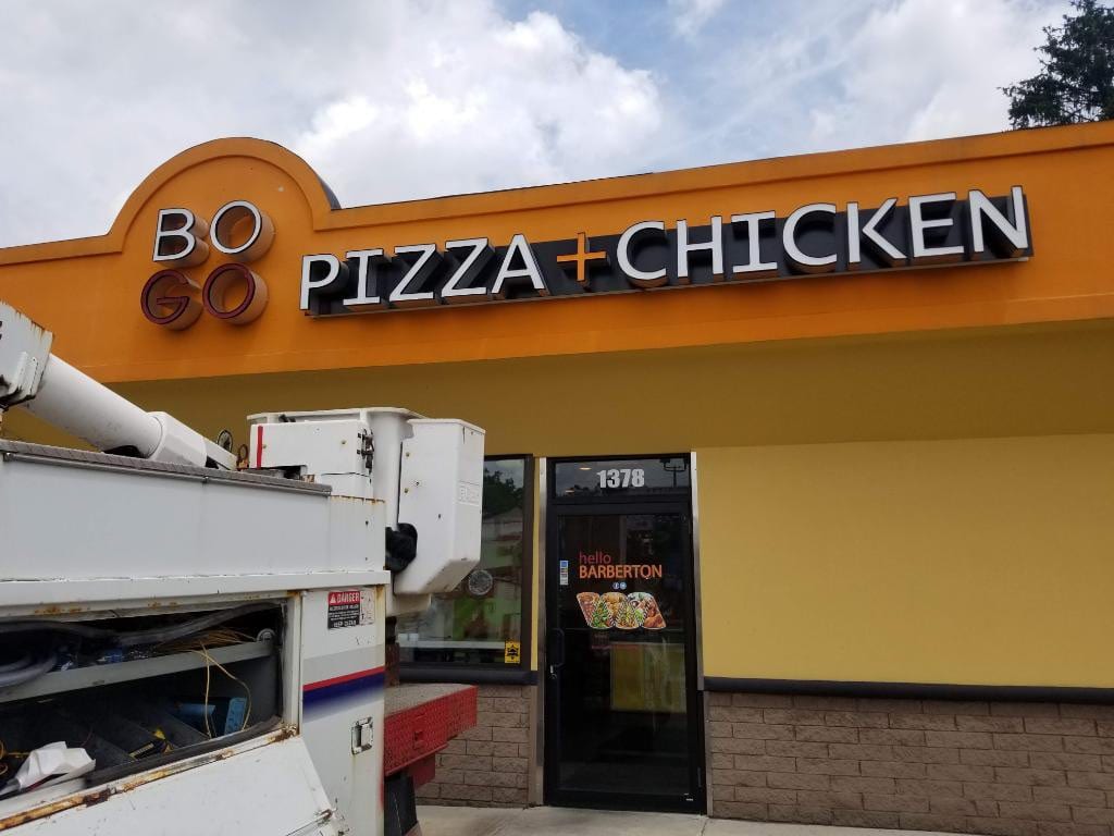 BOGO Pizza + Chicken channel letters on an orange storefront fascia with a bucket truck below