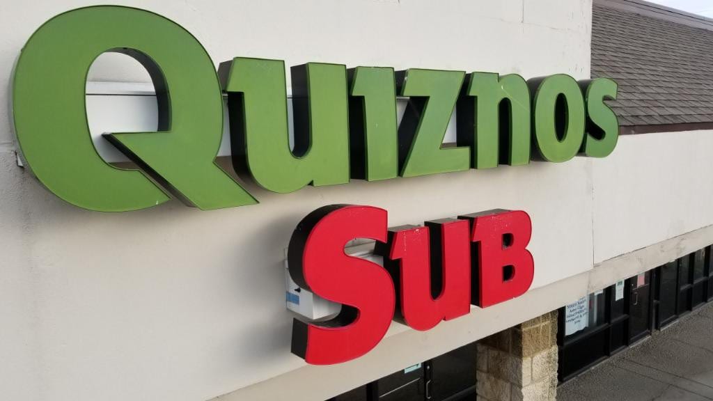 Green and red Quiznos Sub channel letters mounted on a stucco storefront wall