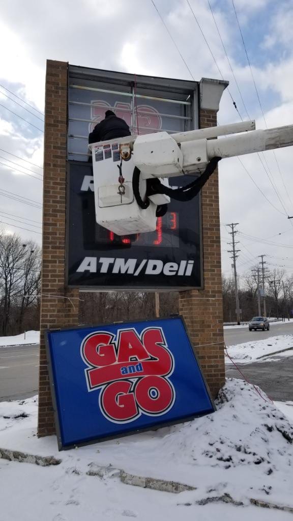 Worker in a bucket lift servicing a Gas and Go pylon sign with the face panel on the ground