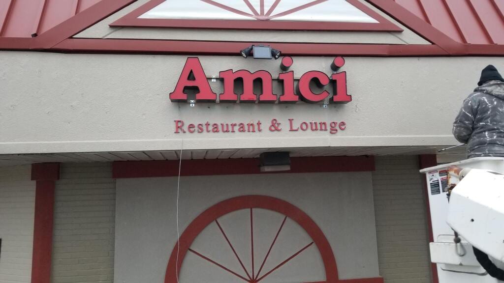 Red Amici Restaurant & Lounge channel letters with a worker in a lift alongside