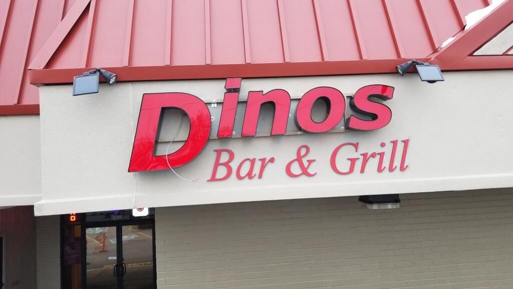 Red Dinos Bar & Grill channel letters lit by gooseneck fixtures on a stucco wall
