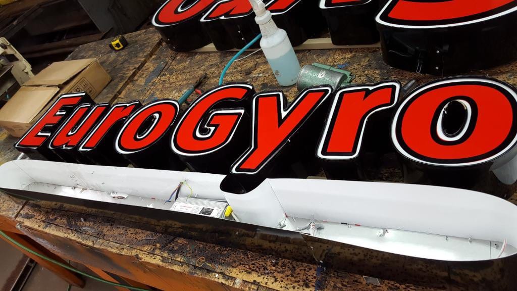 Red EuroGyro channel letters and an open raceway with wiring on a shop workbench