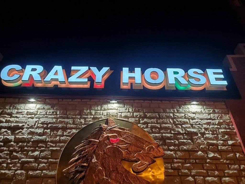 Illuminated CRAZY HORSE channel letters above a stone wall with a metal horse head medallion