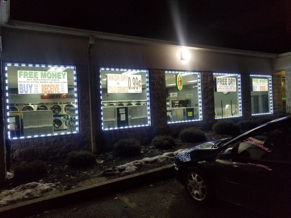 Laundromat windows outlined in LED strips with printed FREE MONEY and wash and fold price signs