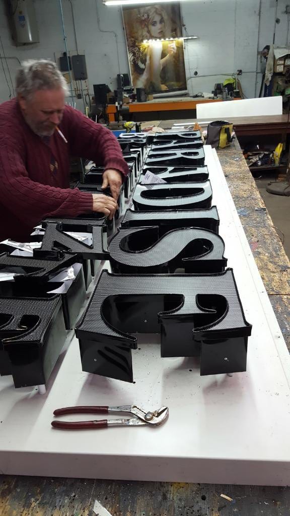 Sign maker assembling black channel letter cans laid out on a shop table
