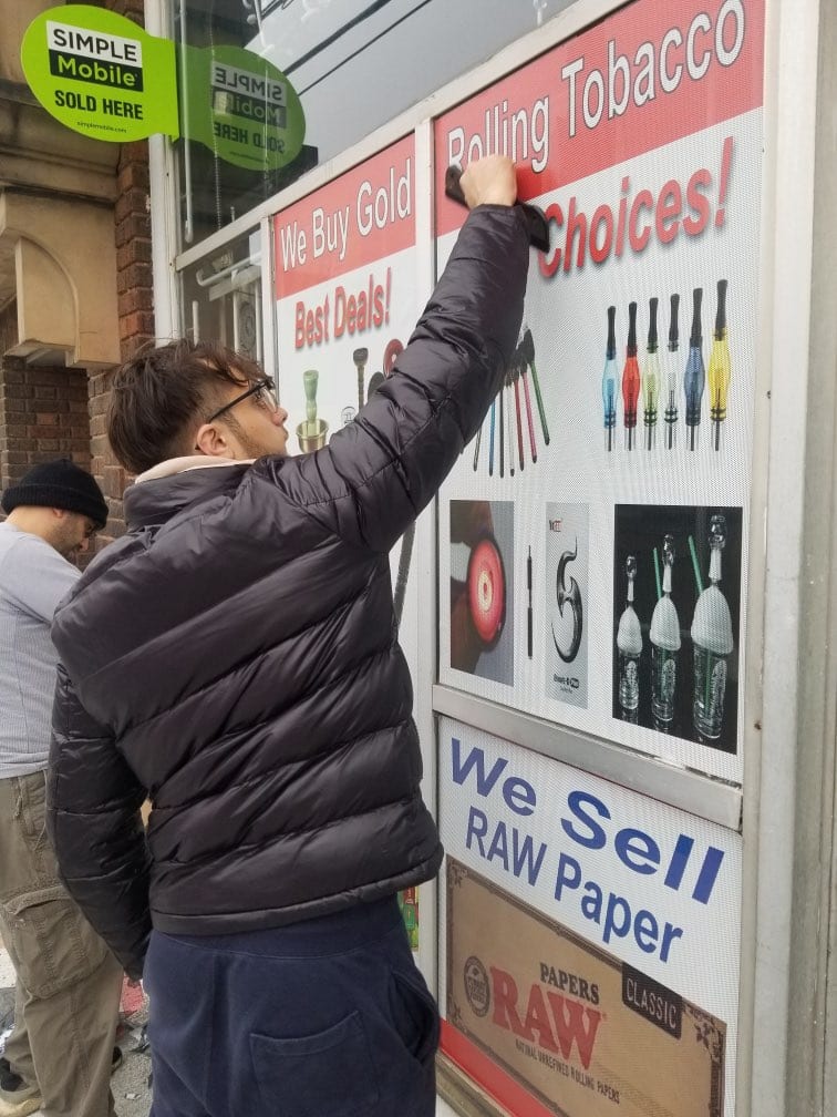 Person at a storefront window covered with printed Rolling Tobacco and We Sell RAW Paper graphics