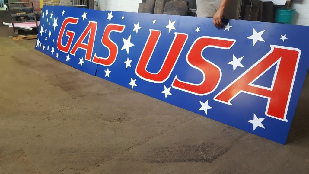 Blue GAS USA sign panels with white stars and red letters leaning inside the fabrication shop