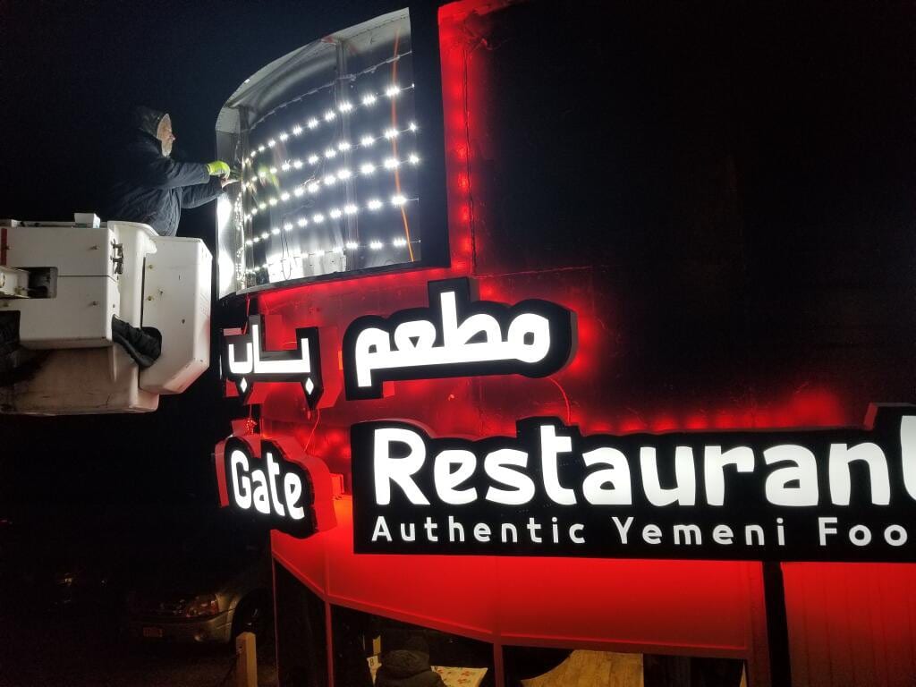 Worker in a lift fitting LED modules above lit Gate Restaurant channel letters at night