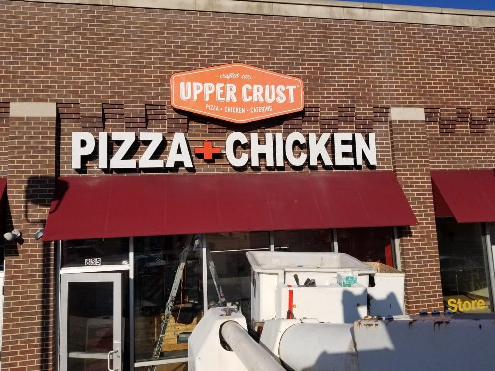 UPPER CRUST PIZZA + CHICKEN letters and logo cabinet on brick with a bucket truck boom below