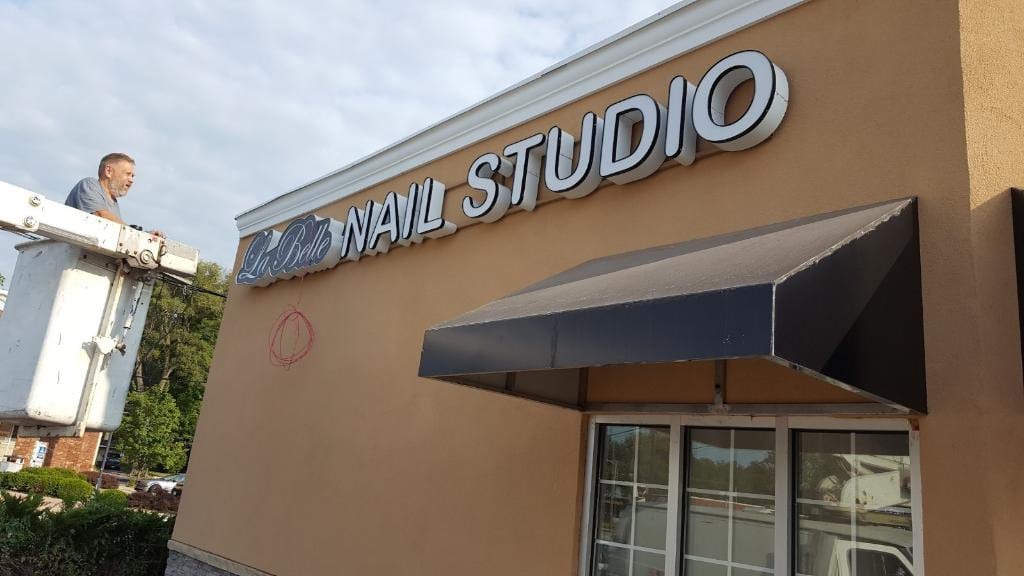 La Belle Nail Studio channel letters on a tan wall with a worker in a bucket lift alongside