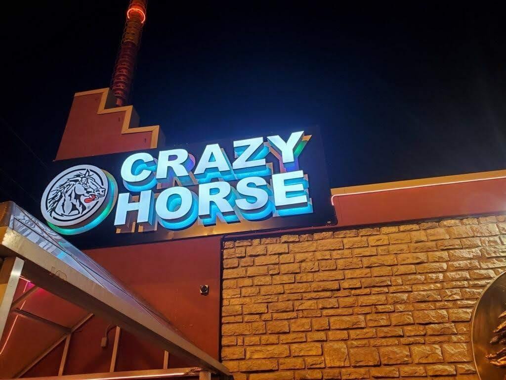 Lit CRAZY HORSE letters and a round horse logo on a dark fascia above stone at night
