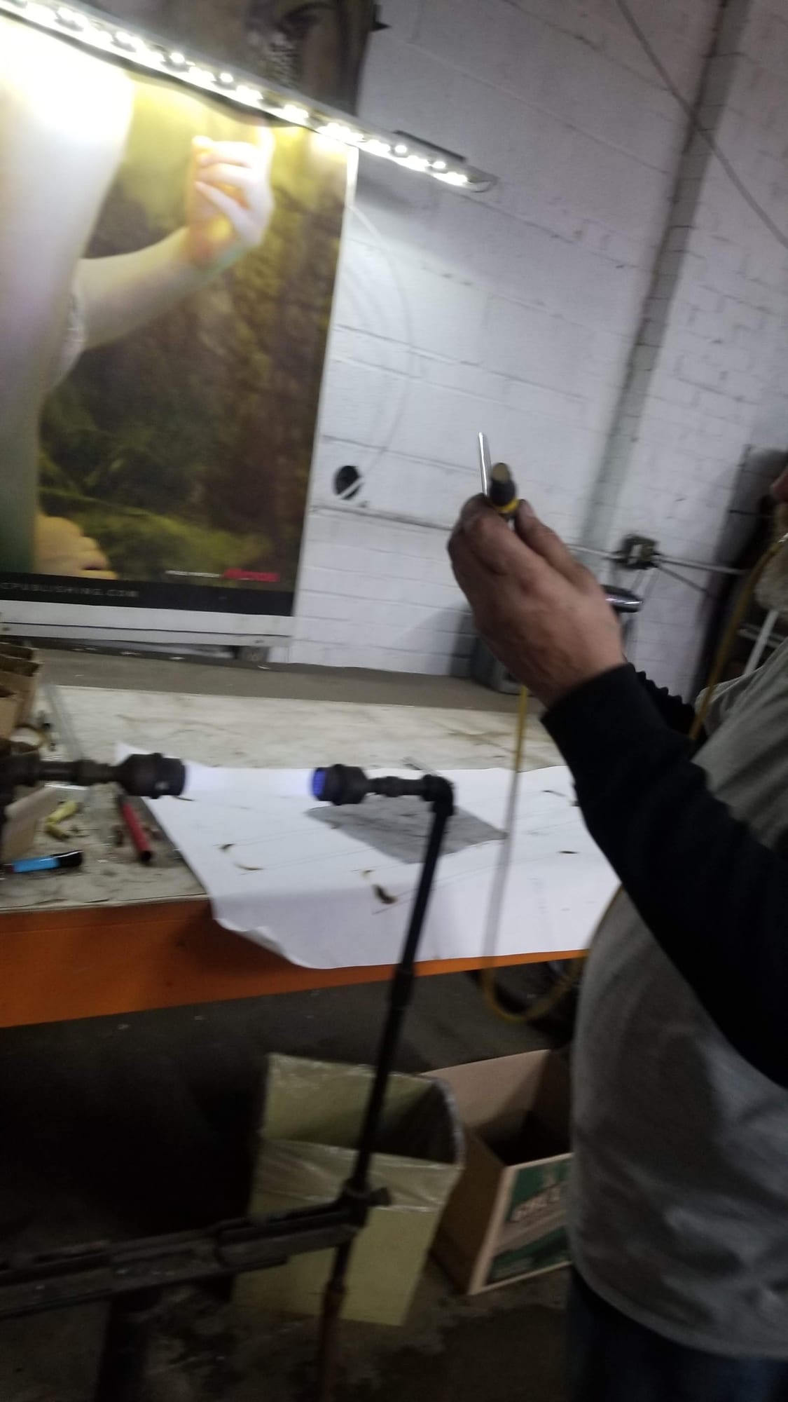 Sign maker holding a glass tube beside a bench burner in a dim workshop