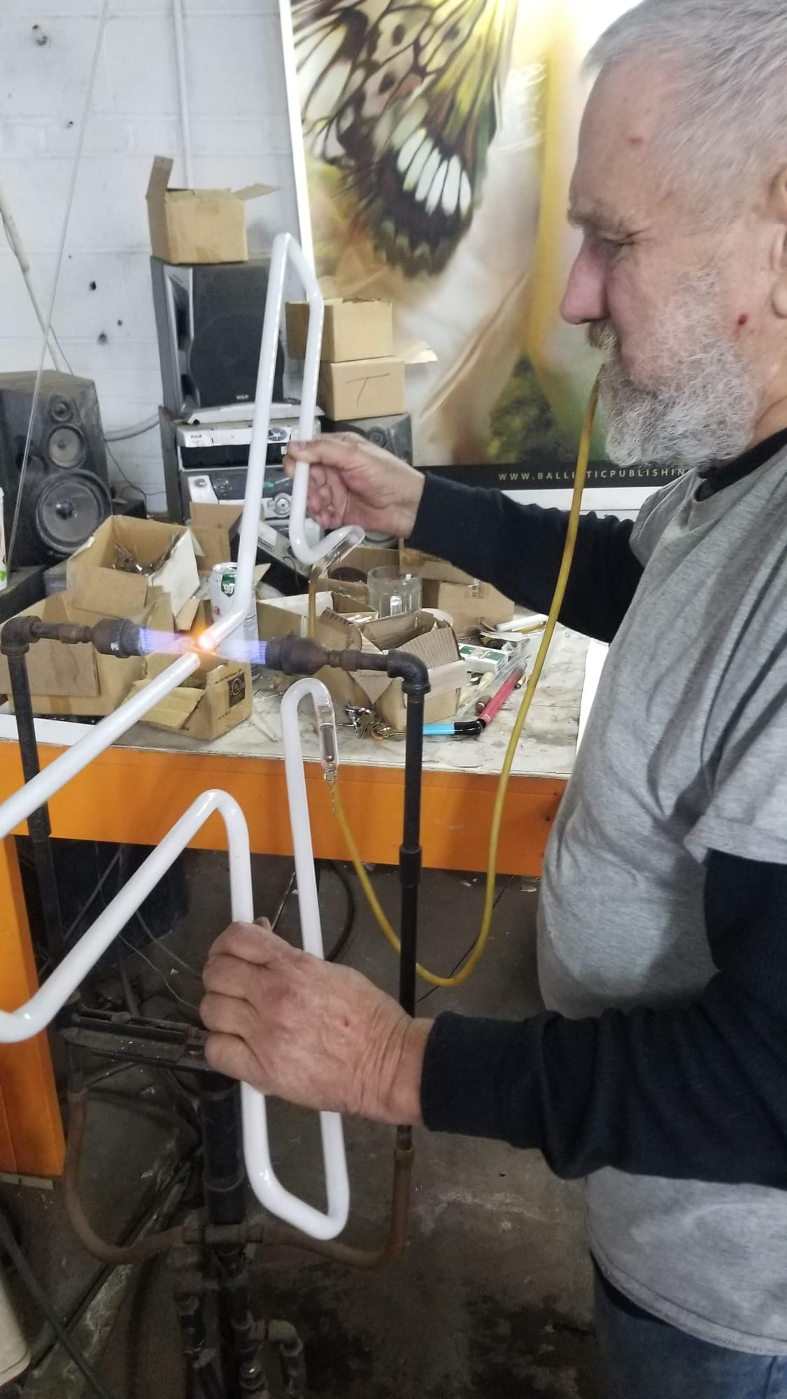 Neon glass bender heating a white tube over a burner flame at a shop bench