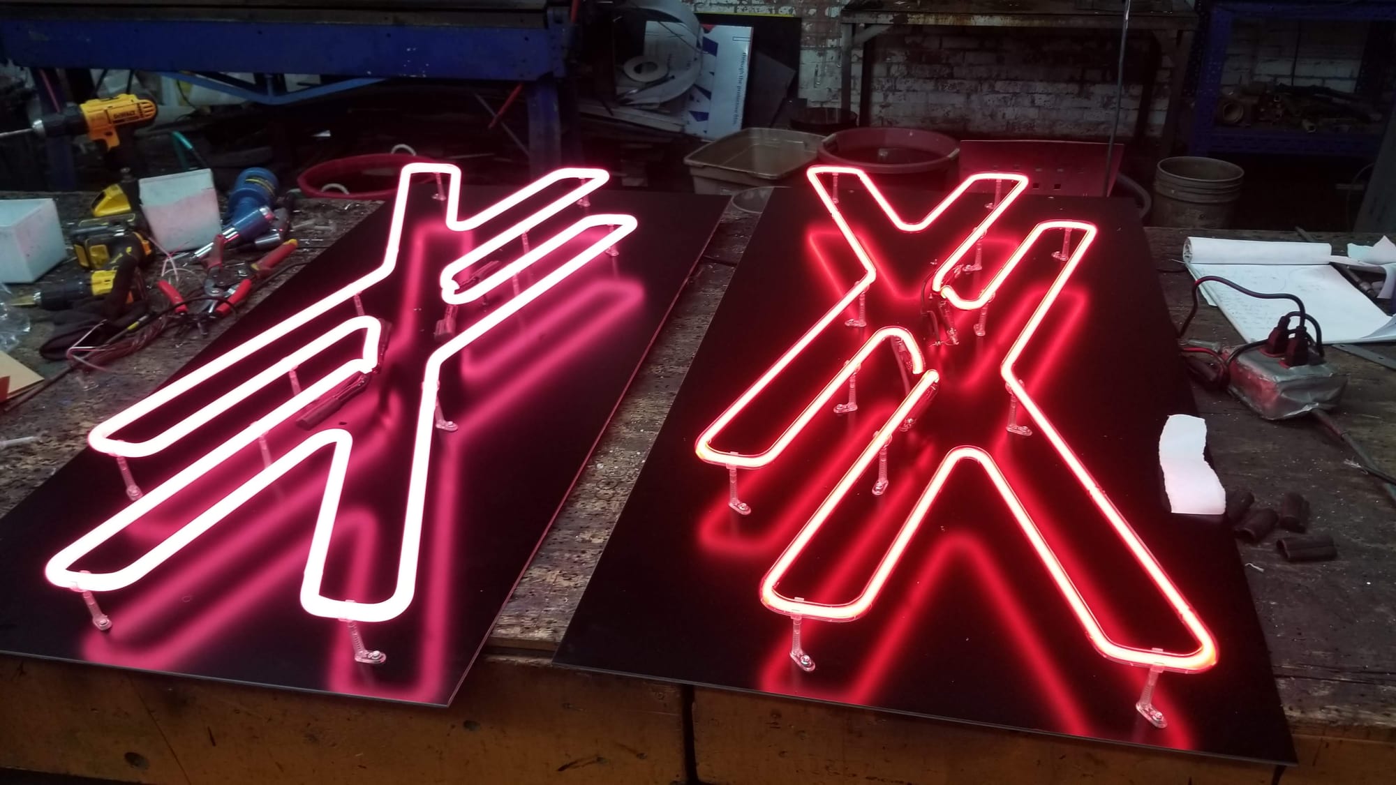 Two red neon letter units lit and mounted on black panels at a workshop bench