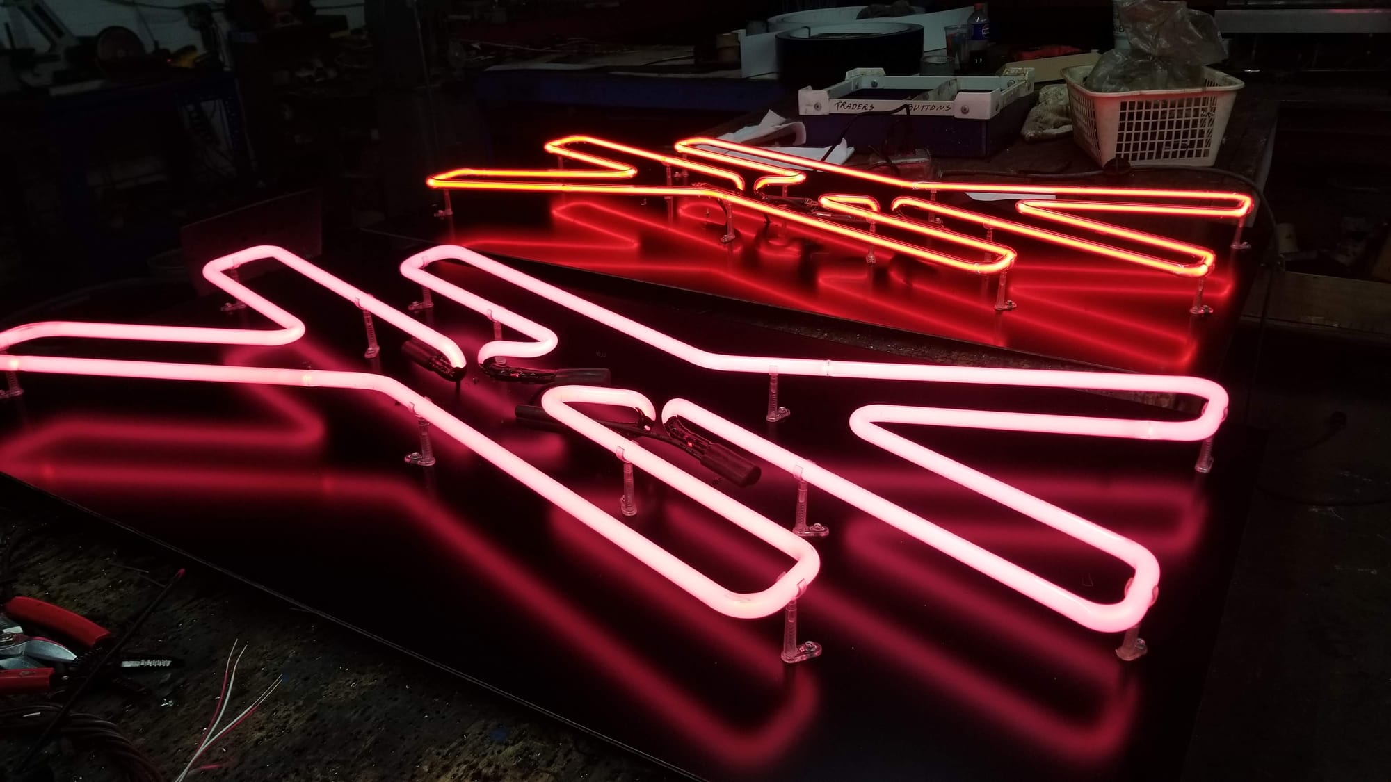 Several red and pink neon letters glowing on black panels in the shop