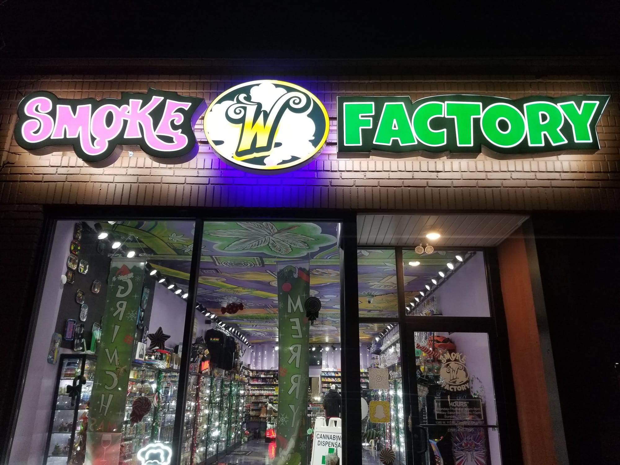 Illuminated SMOKE FACTORY shaped cabinet signs with purple halo glow above a shop at night