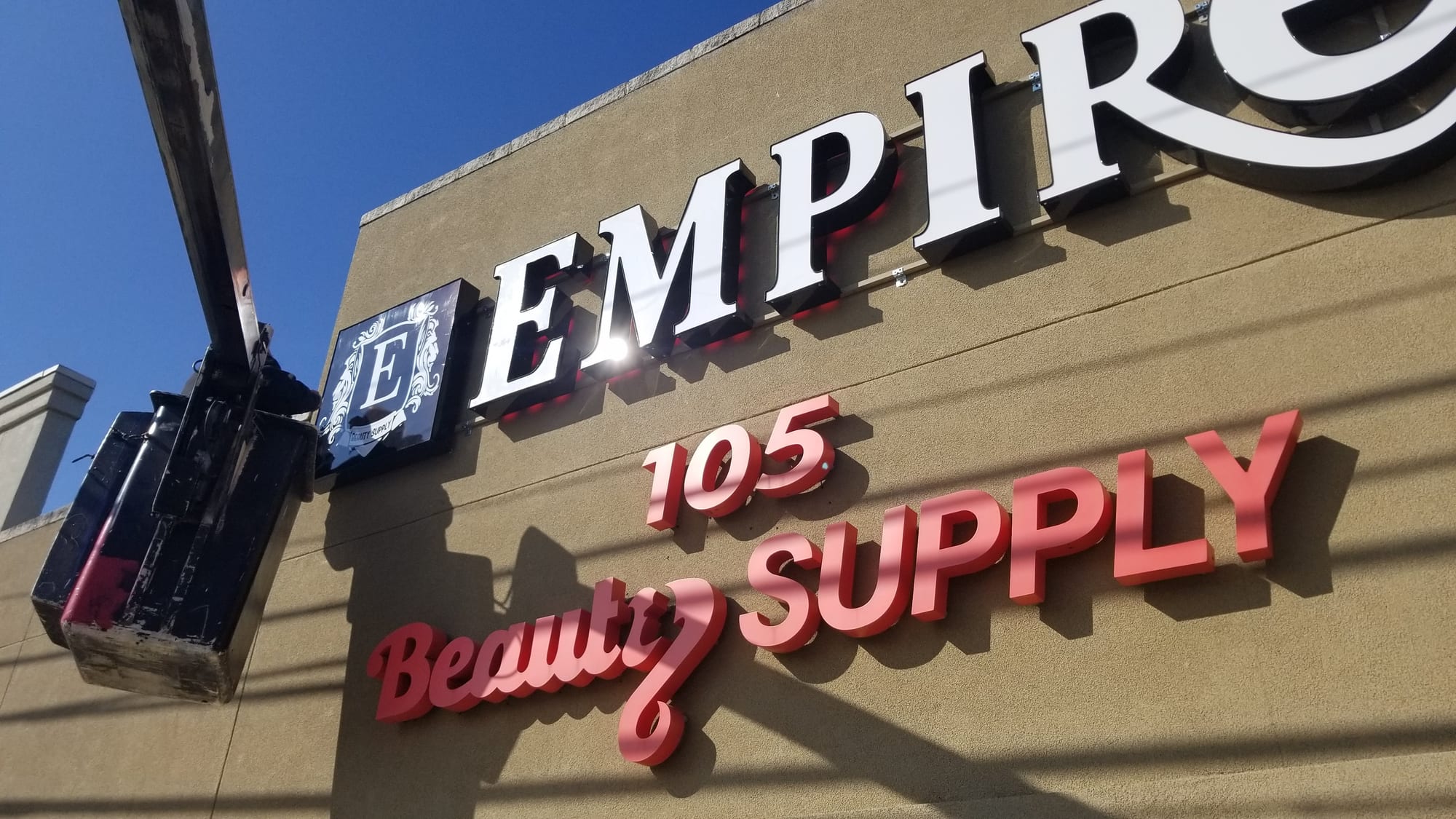 Empire Beauty Supply lit letters and red dimensional lettering with a bucket lift alongside