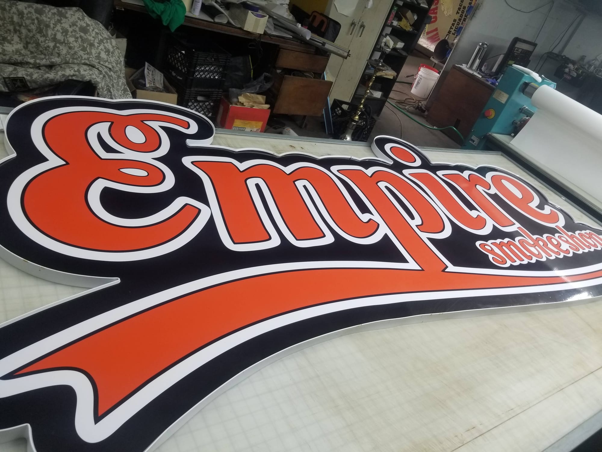 Shaped Empire Smokeshop sign face in orange script resting on a shop table