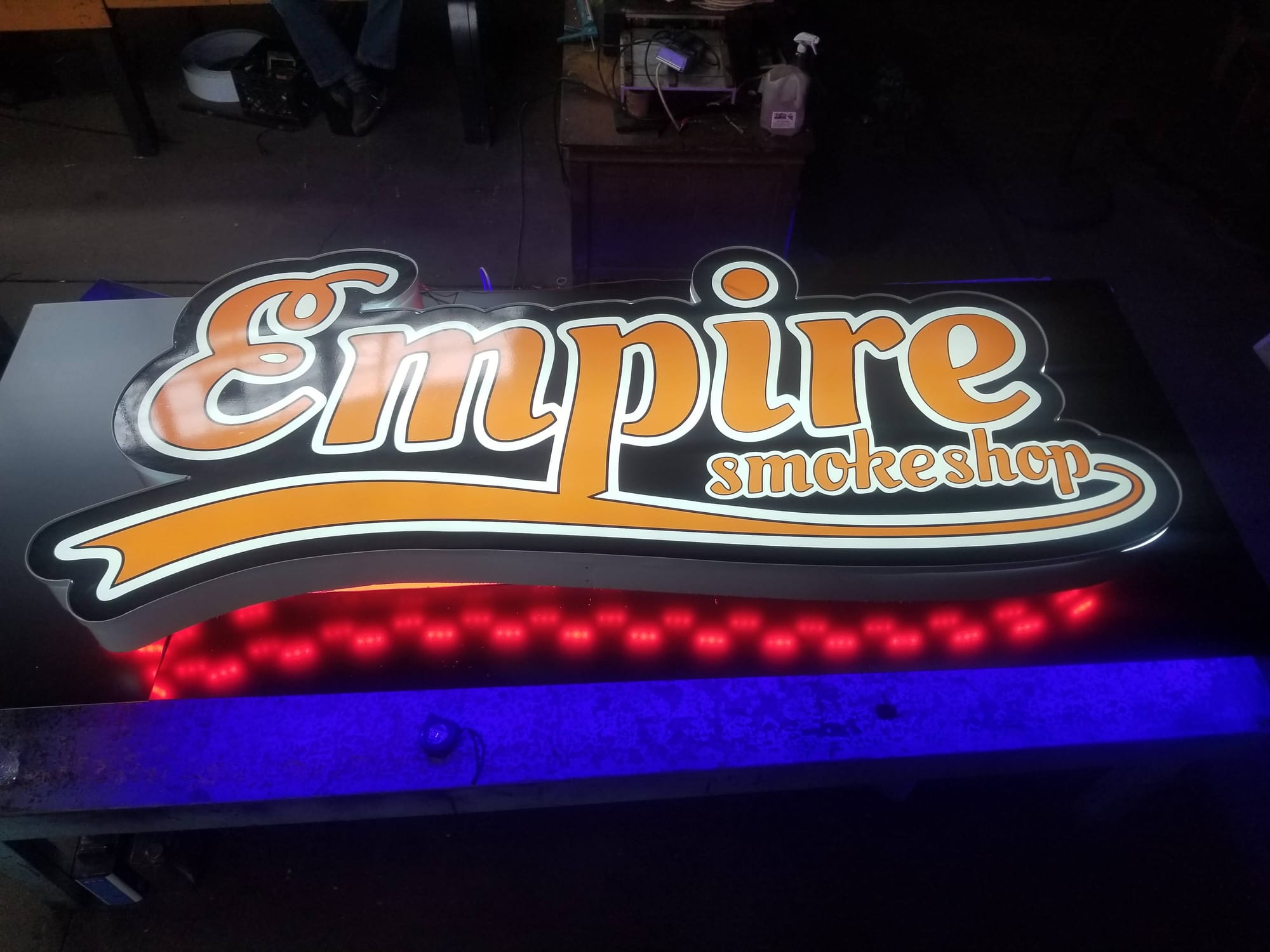 Illuminated shaped Empire Smokeshop cabinet sign lit on a bench with red LEDs below