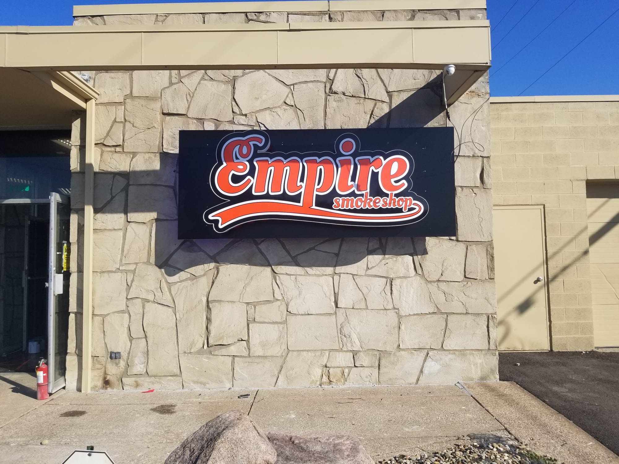 Empire Smokeshop illuminated cabinet sign mounted on a stone storefront wall