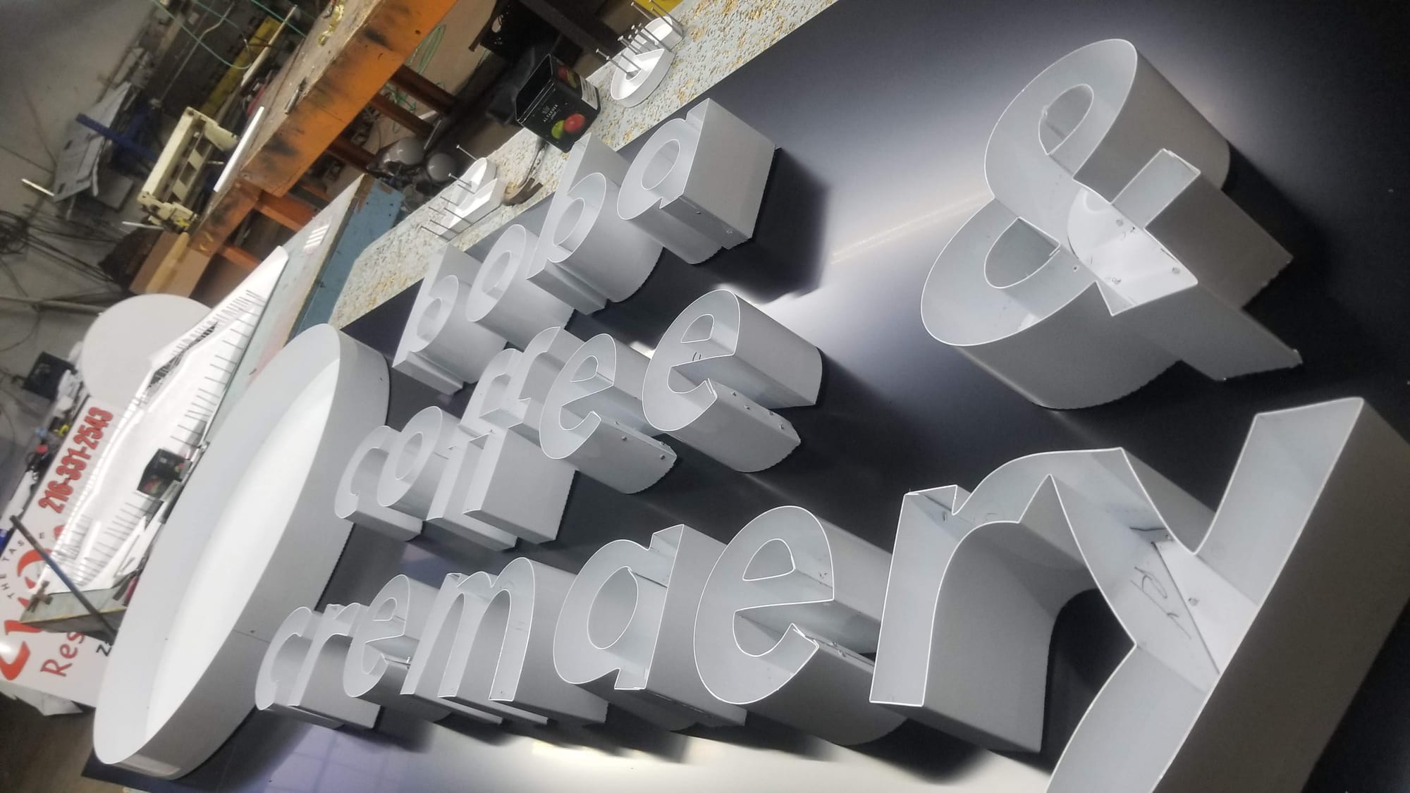Unfinished white channel letters reading boba coffee and creamery laid out in the sign shop