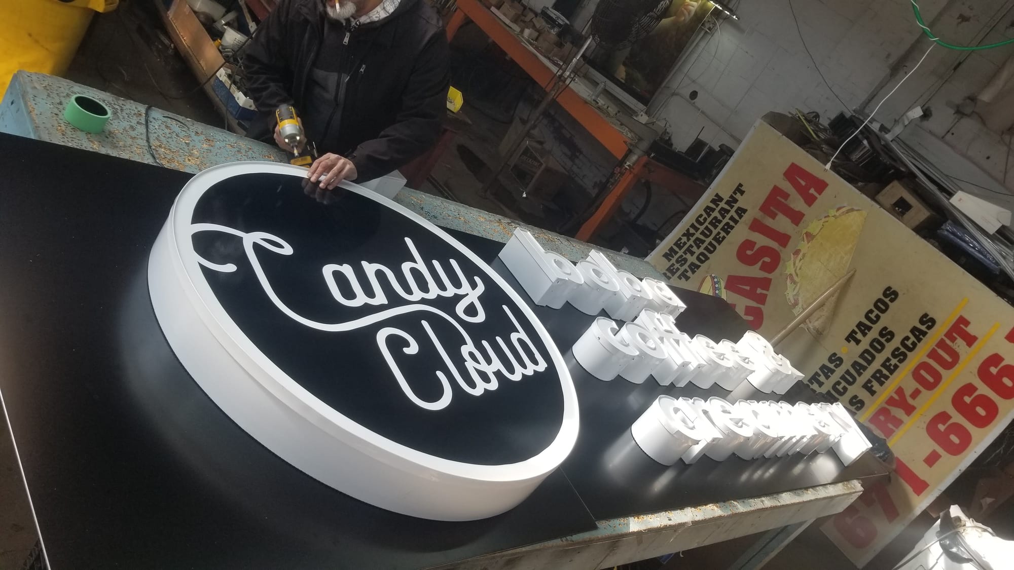 Worker drilling the Candy Cloud oval cabinet and channel letters on a shop bench