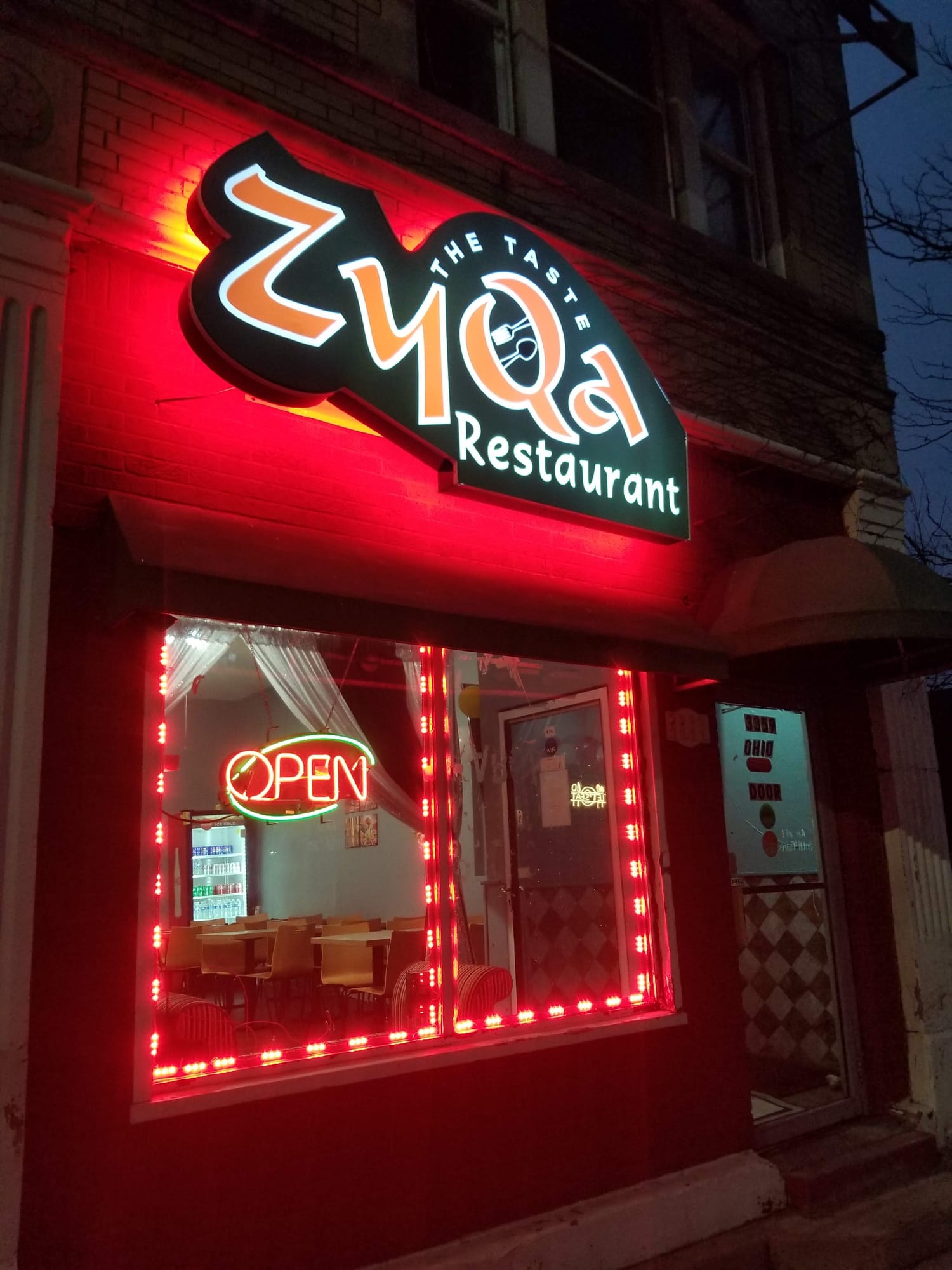 Lit ZyQa Restaurant shaped cabinet sign glowing red above a storefront window at night
