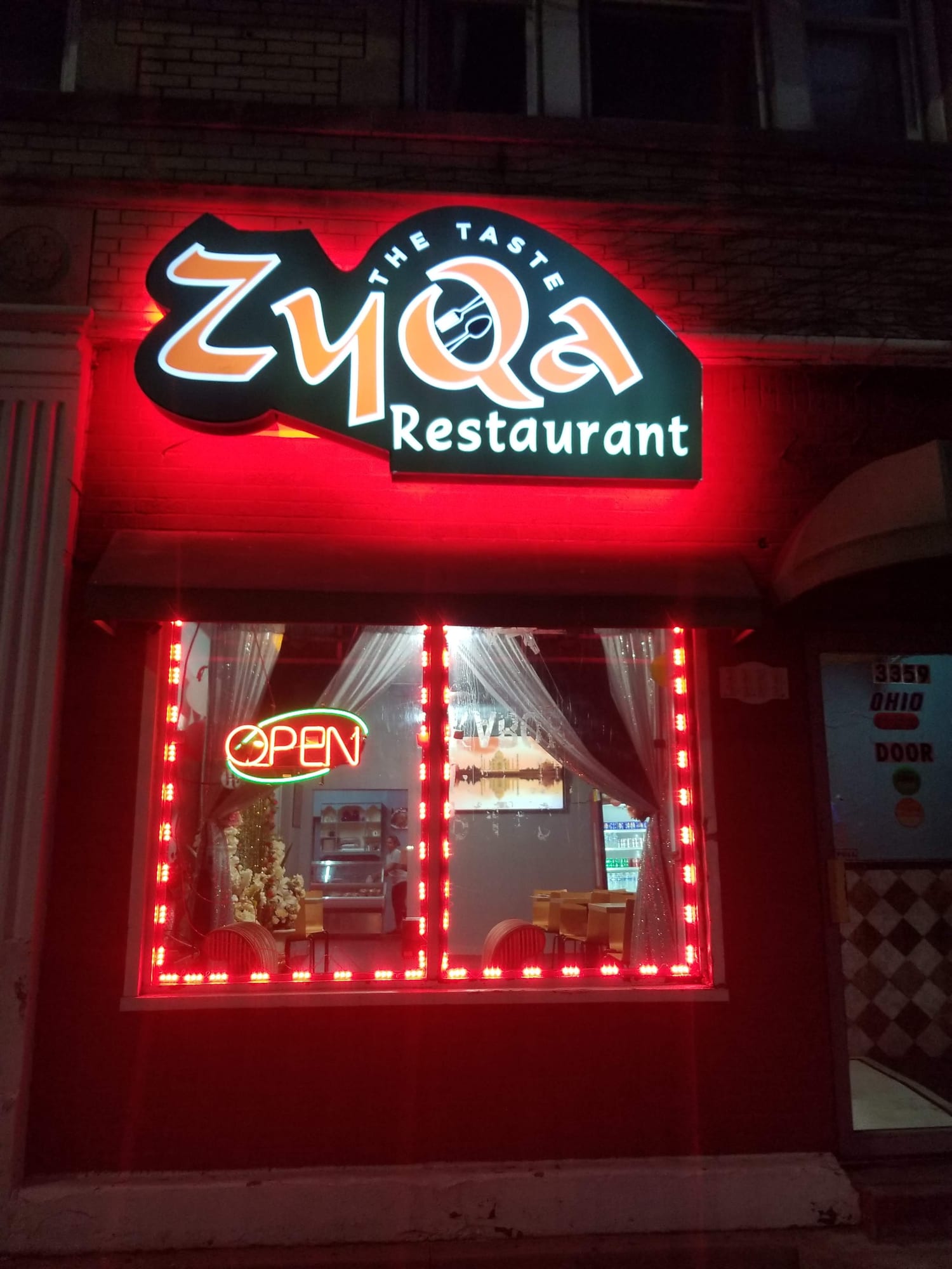 ZyQa Restaurant illuminated cabinet sign lit at night over the restaurant window
