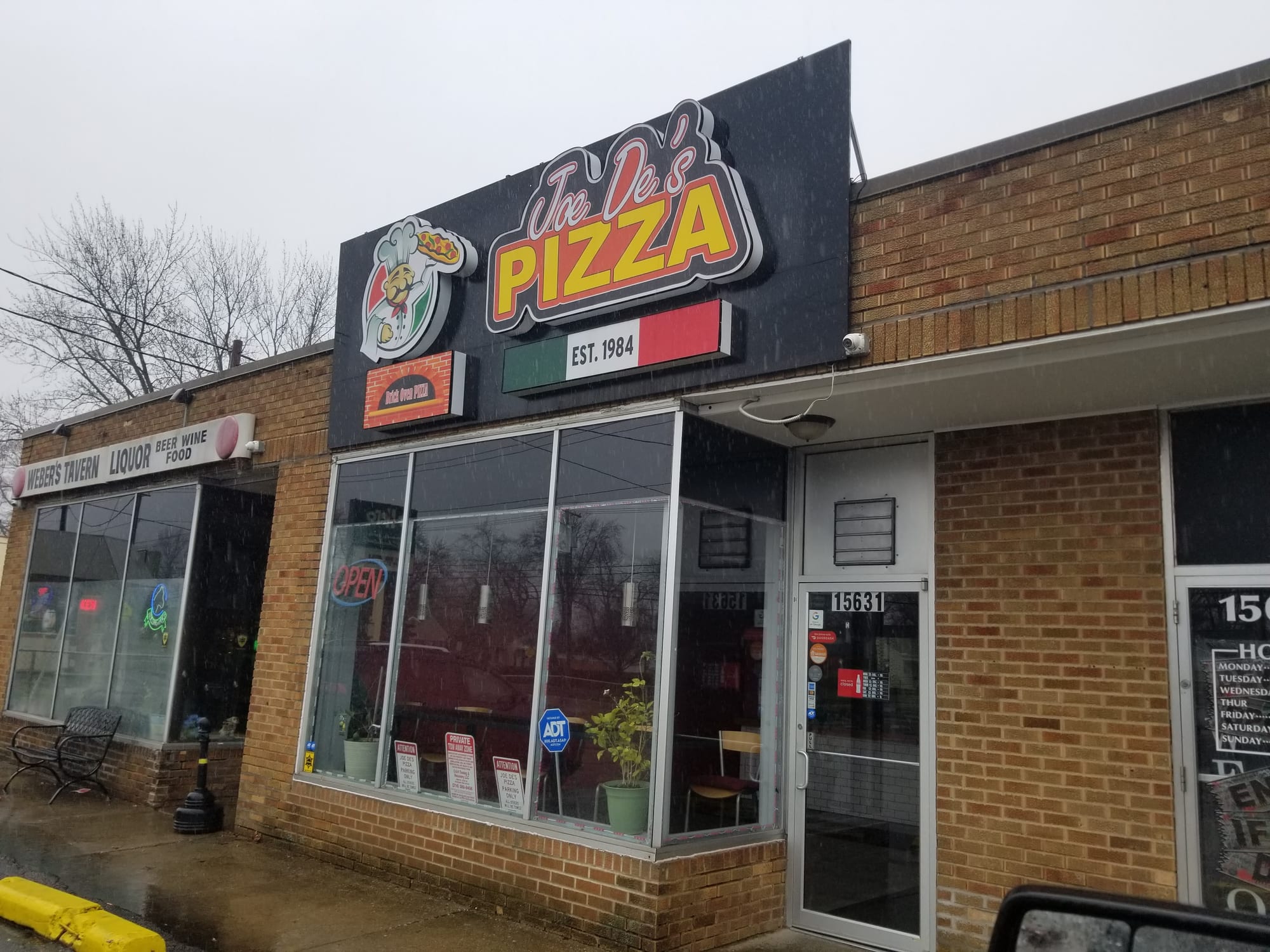Joe De's Pizza shaped cabinet sign above a storefront on a rainy day