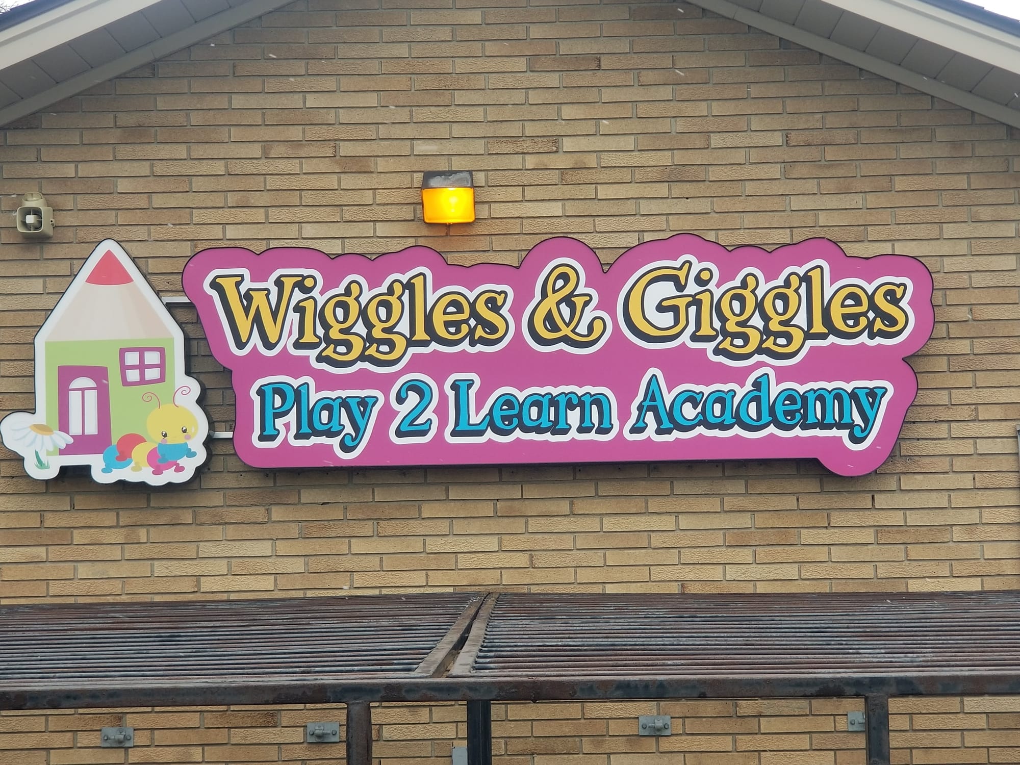 Wiggles and Giggles Play 2 Learn Academy shaped sign panel mounted on a brick wall