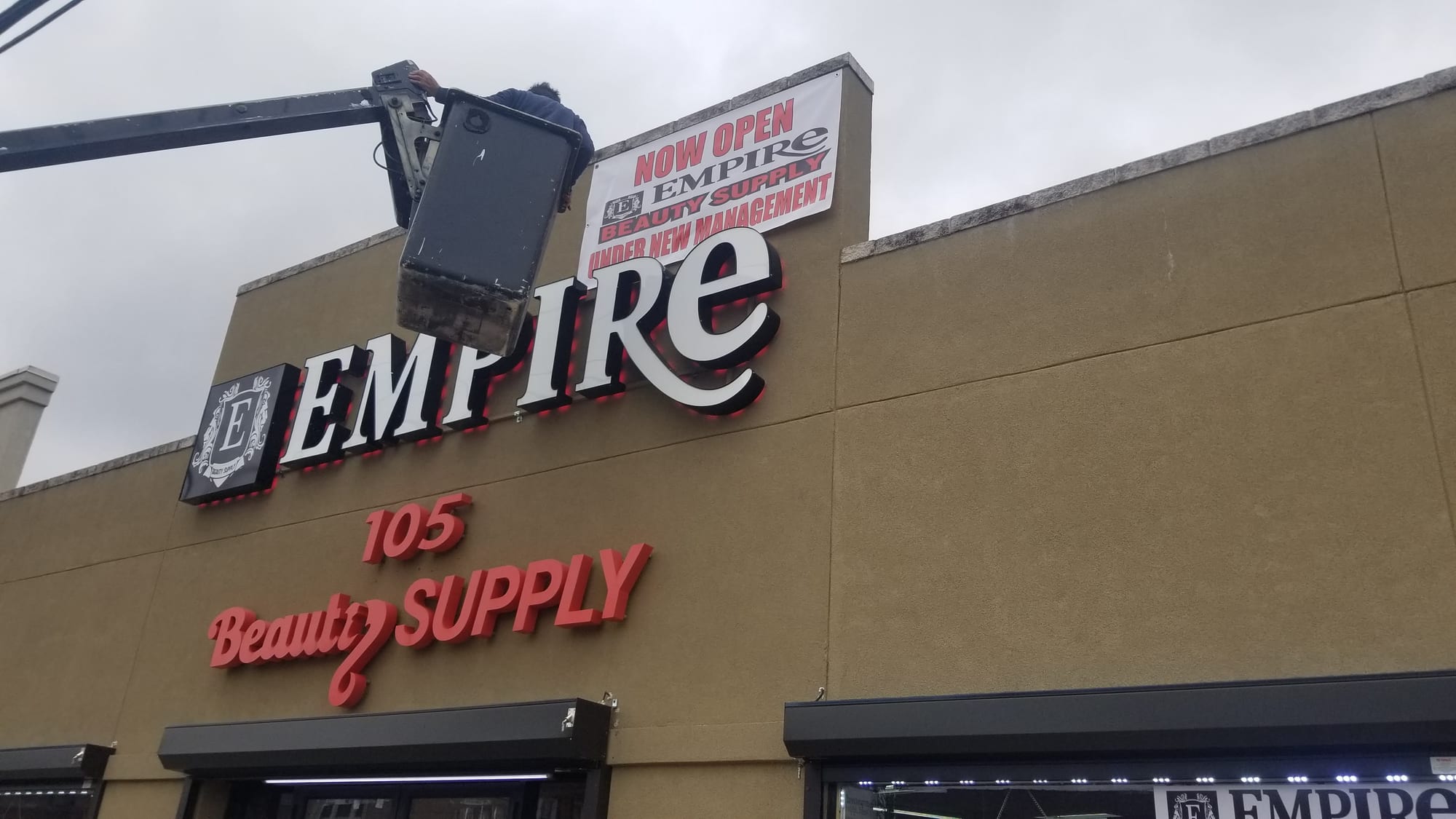 Installer in a bucket lift working on lit Empire Beauty Supply letters on a building